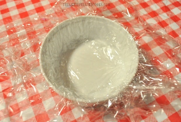 A ramekin with plastic wrap, is prepared for Mom's famous cream cheese ball mixture.