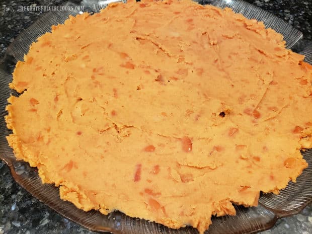 Refried beans are spread out onto a large round serving platter.