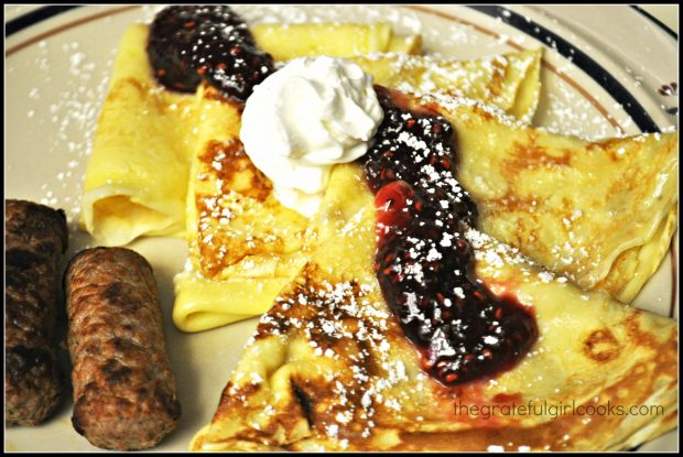 Several Swedish pancakes on plate with link sausage on the side.
