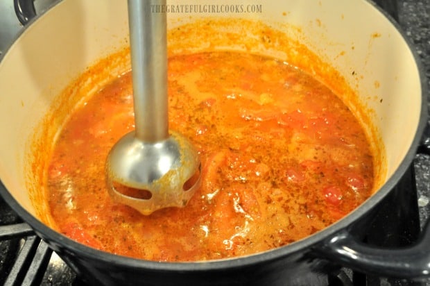 Using an immersion blender to puree the tomato soup.