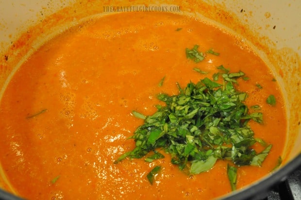 Fresh, chopped basil is added to tomato soup, then blended in.