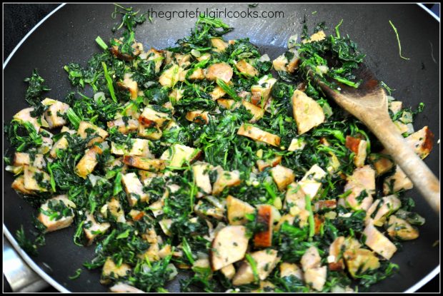 Spinach and garlic are added to the skillet of sausage and onions.