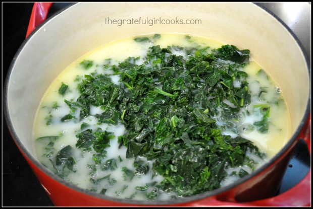 Chopped kale is added to the soup in pan.