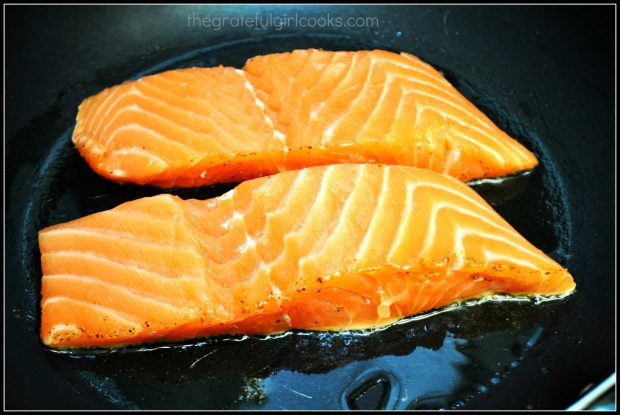 The salmon fillets are pan seared, seasoned side down, in hot oil.