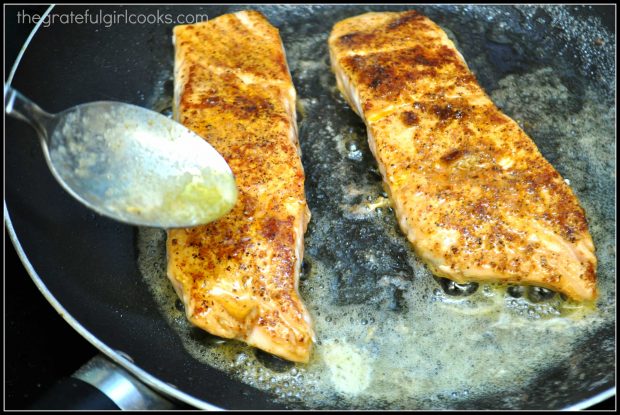 Salmon, seasoned with Cajun seasoning, cooking in a skillet.