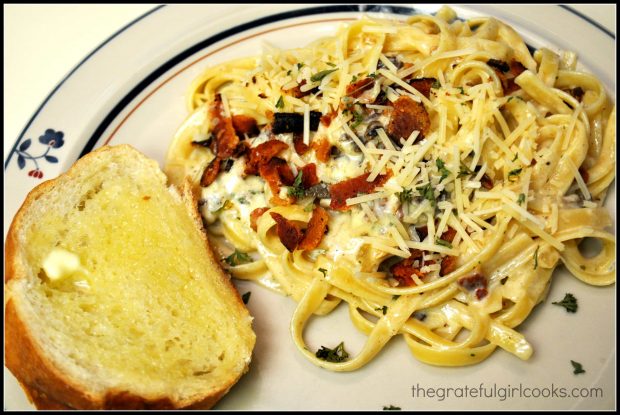 A plate with a serving of pasta carbonara, and a slice of french bread.