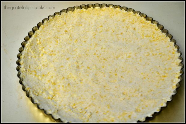 A shortbread crumble mixture is pressed into a metal tart pan to form a firm crust.