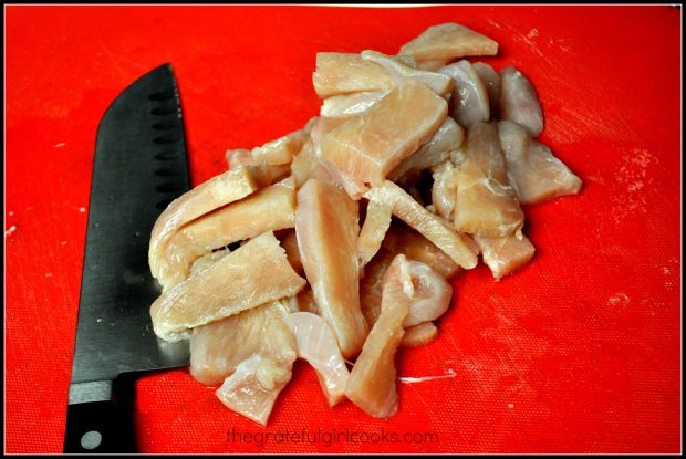 Chicken breast slices, with knife on red cutting mat.
