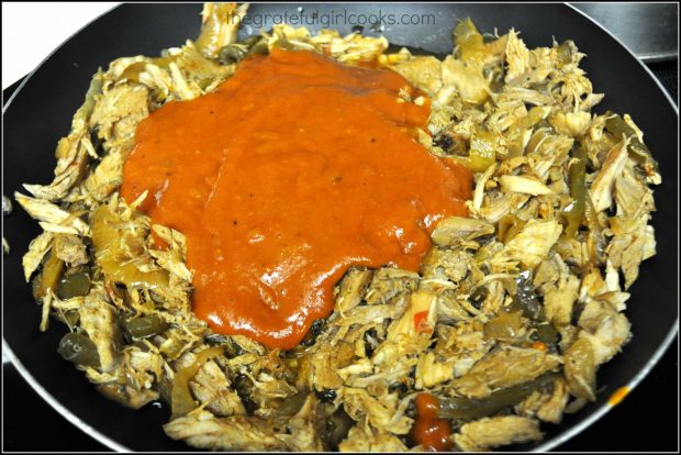 Homemade red sauce is added to shredded pork burrito filling in skillet, to season.