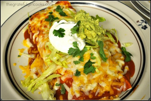 Shredded Pork Smothered Burritos are garnished with sour cream, guacamole, lettuce and cilantro for serving.
