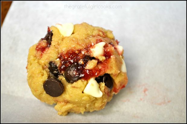 A close up view of a cookie (before baking), with raspberry jam and chocolate chips showing.