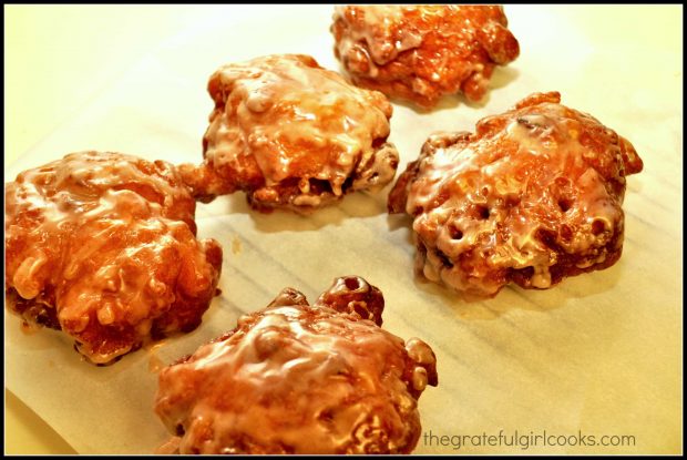 Fritters coated with a glaze, resting on parchment paper