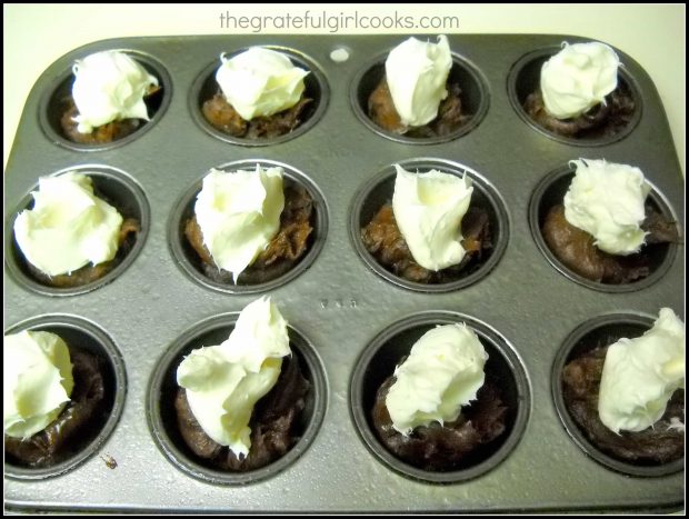 Cheesecake filling is dolloped onto the brownie batter in the muffin cups.