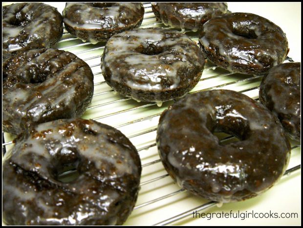 Glazed chocolate doughnuts cooling on wire rack after being iced.