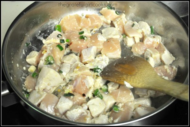 Chicken, garlic and green onions are cooked through in a large skillet.