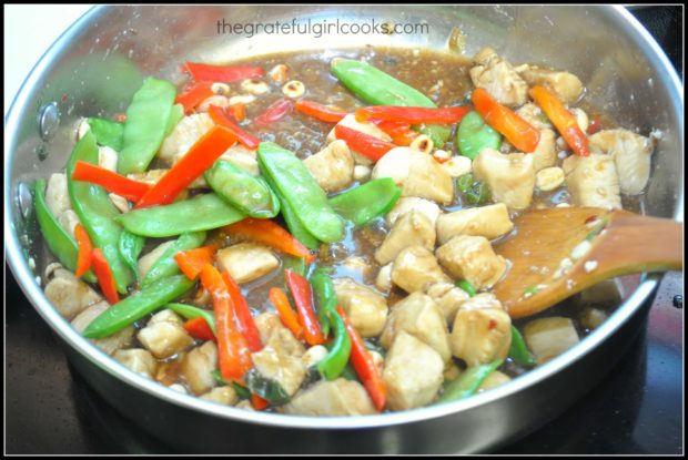 Veggies, sauce, and dry roasted nuts are added to healthy kung pao chicken in skillet.