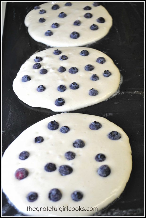 Homemade blueberry pancakes cooking on griddle.
