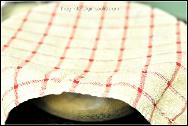 Dough for honey oat bread is rising in glass bowl with dish towel on top