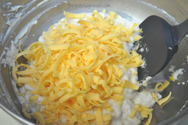 Grated cheese and milk are added to the dry ingredients in the bowl.