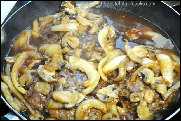 Salisbury Steak is in skillet, topped with mushroom/onion gravy to cook.