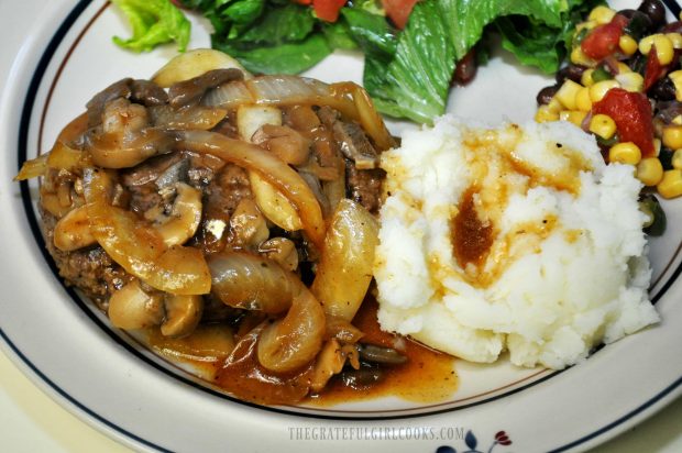 Salisbury Steak is served on plate with mashed potatoes and salad on the side.