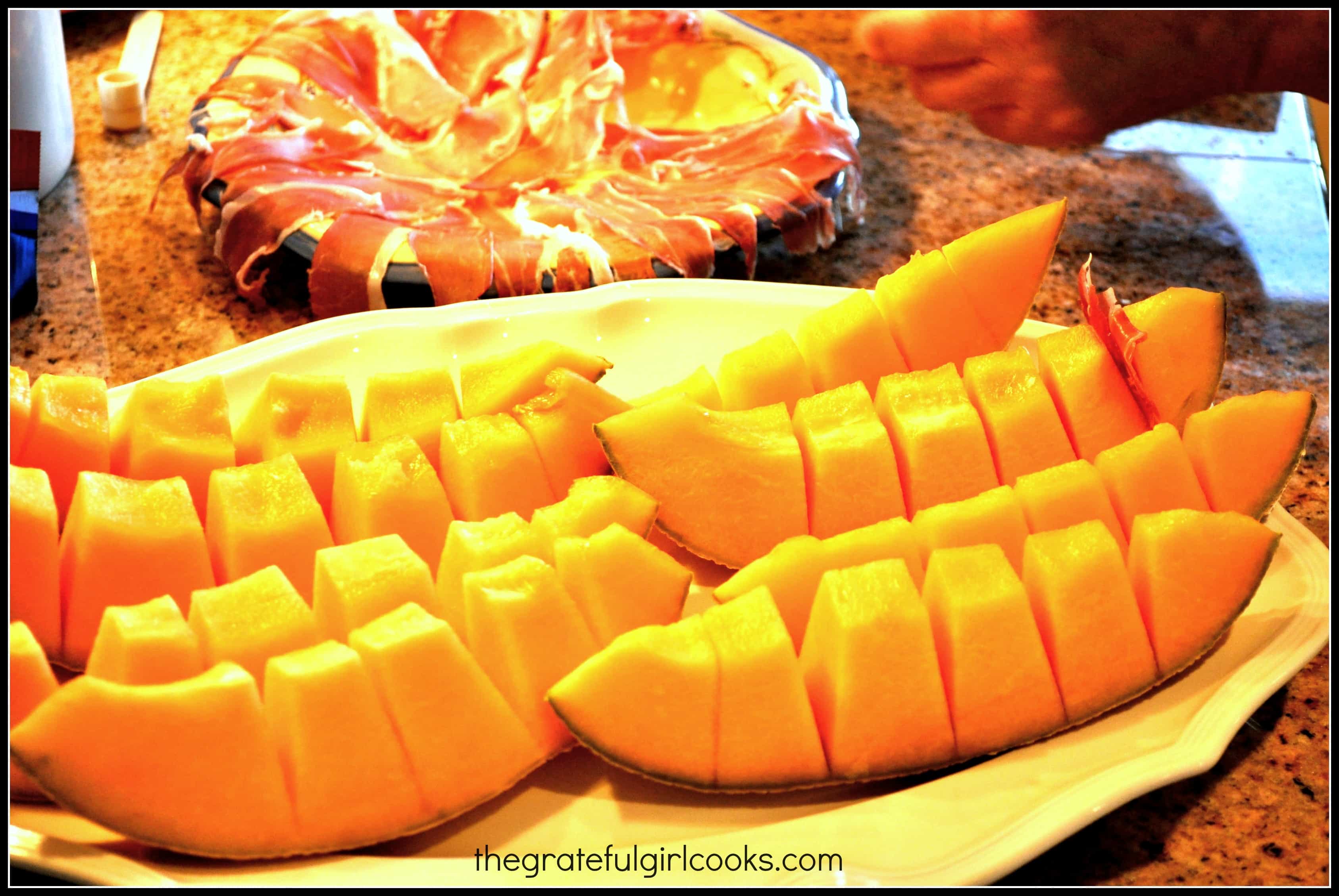 Cantaloupe cut into slices, with prosciutto slices in background