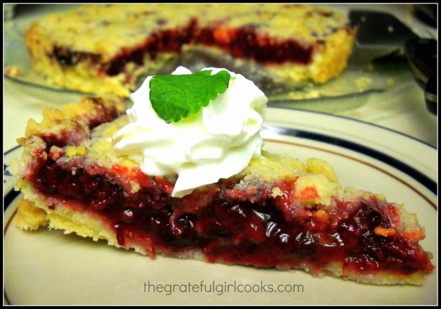 Slice of boysenberry shortbread tart on plate, served with whipped cream