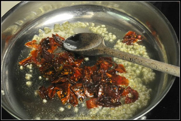 Sun-dried tomatoes and red chili flakes are added to the garlic in the skillet.