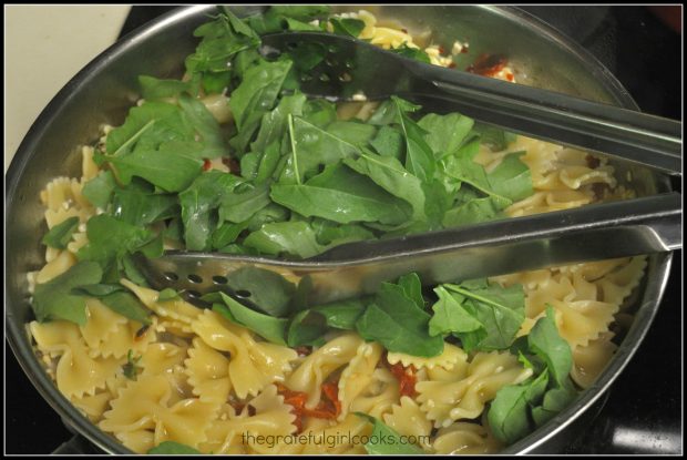 Drained pasta and arugula are added to the skillet.