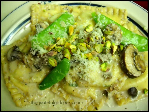 Finished ravioli with mushrooms is garnished with chopped pistachios and Parmesan cheese.