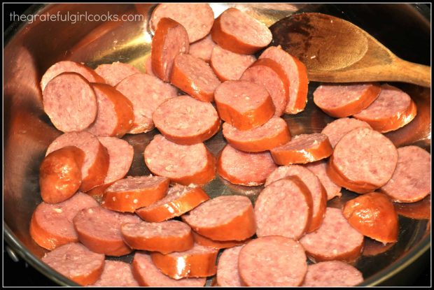 Cooking polska kielbasa slices in a large skillet until lightly browned.