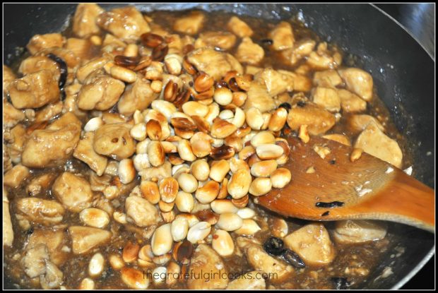 Toasted peanuts are added to kung pao chicken in skillet.