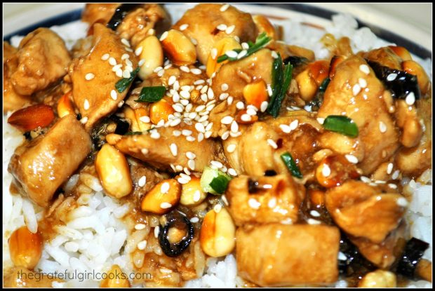 Kung Pao Chicken is garnished with sesame seeds and green onions, and is served on rice.