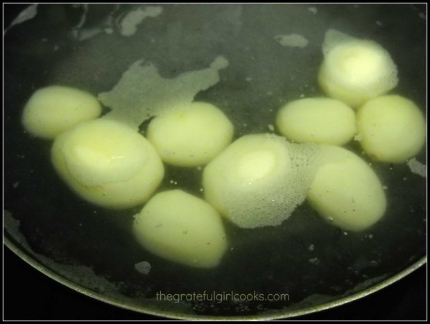 Peeled, baby red potatoes are boiling in water in pan, to make rissole potatoes.