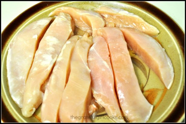 Raw chicken breast strips on platter