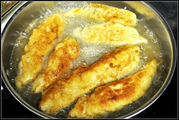 Strips of chicken frying in oil in skillet