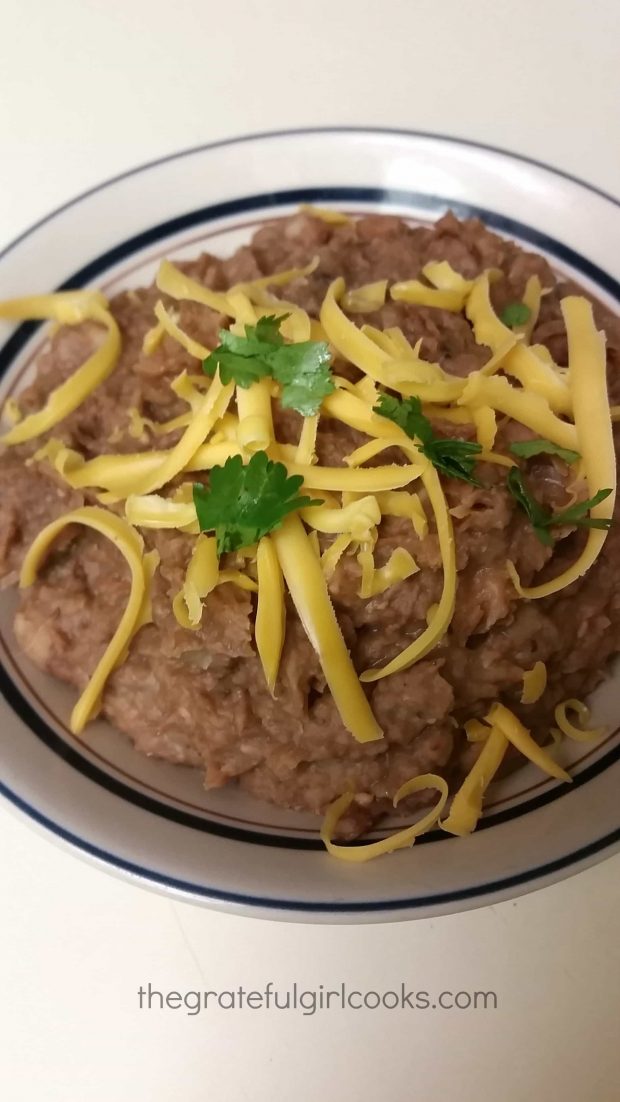 Crock pot refried beans are served with a garnish of grated cheddar cheese and cilantro.