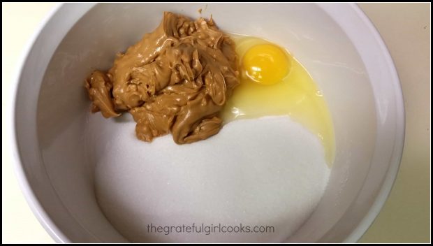 Ingredients for cookies (peanut butter, eggs, and sugar), in white bowl