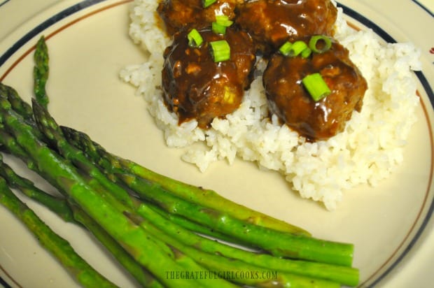 Hoisin Asian Meatballs are served as a main dish, on a bed of rice, with asparagus on the side.
