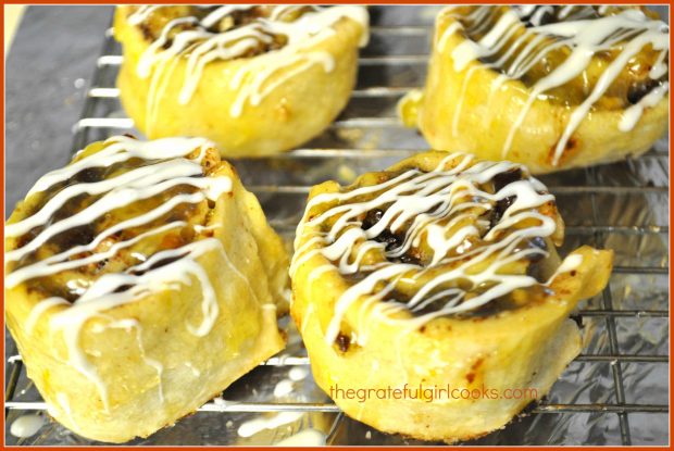 Cranberry-orange pinwheels with white chocolate drizzle, cooling on wire rack.