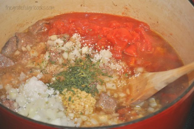 Tomatoes, onions, garlic and spices are added to classic beef stew in pan.