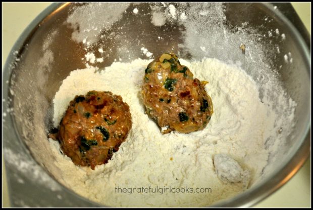 All of the browned meatballs are coated in flour in small bowl.