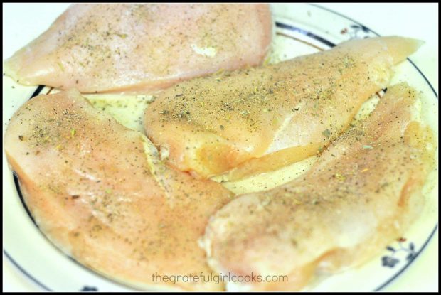 Four raw seasoned chicken breasts on plate
