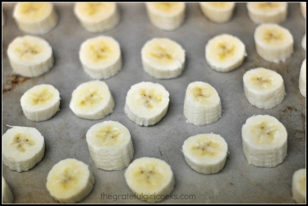 Sliced frozen bananas on a cookie sheet are ready to make chocolate dipped frozen banana bites.