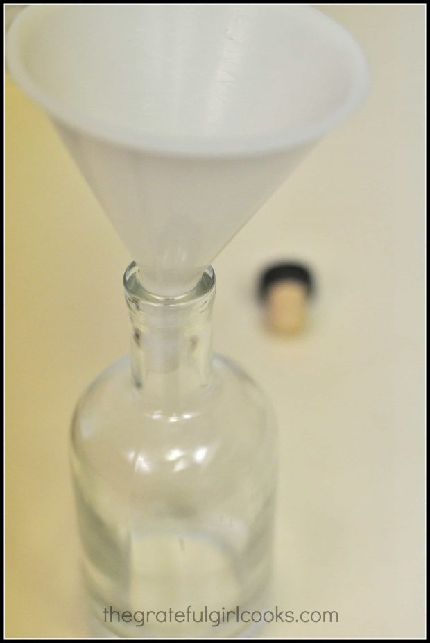 The homemade amaretto is transferred into a bottle by using a funnel.