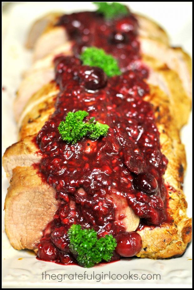 Baked pork tenderloin is served with cranberry-raspberry sauce on top.