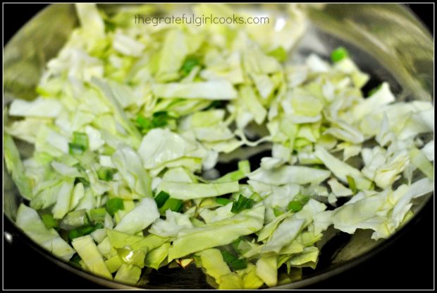 Shredded cabbage and green onions are cooked in skillet.