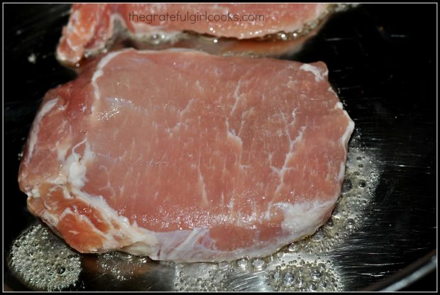 Pork chops are seared in skillet until lightly browned before baking.