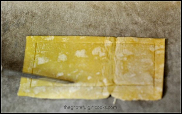 Each pastry dough piece is scored with a knife around the edges.