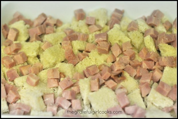 Bread cubes are topped with ham cubes for breakfast souffle.